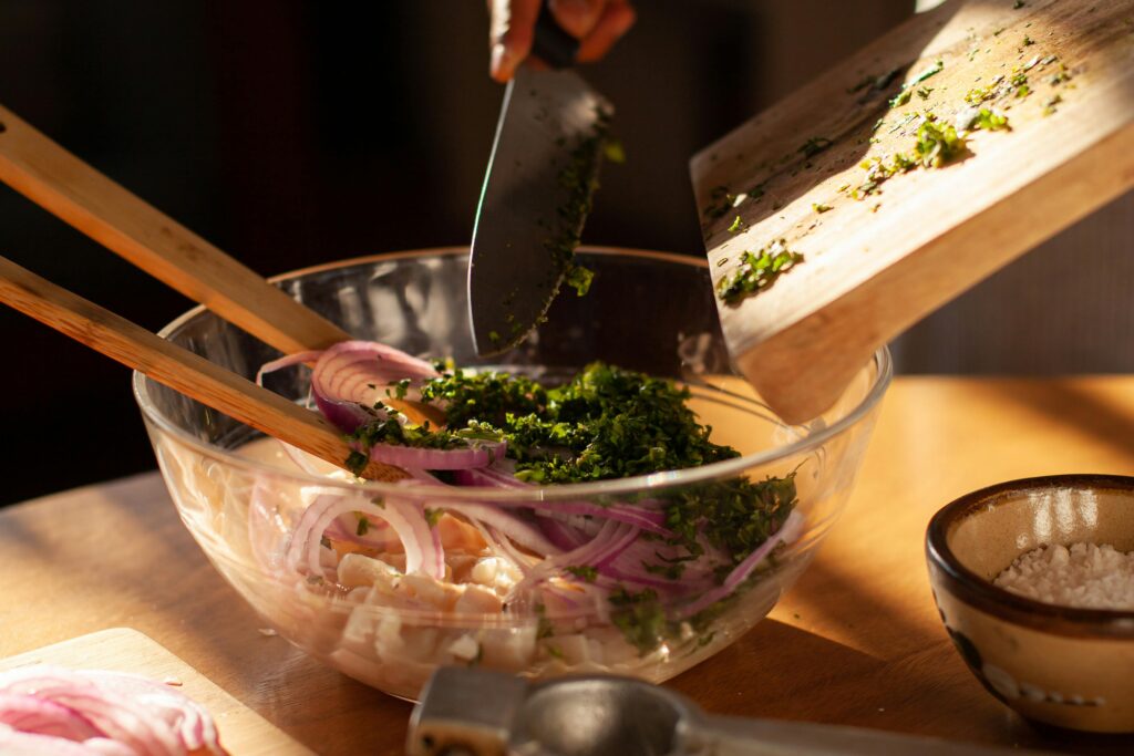 A vibrant salad preparation with chopped onion and herbs in a clear bowl, set on a wooden table.